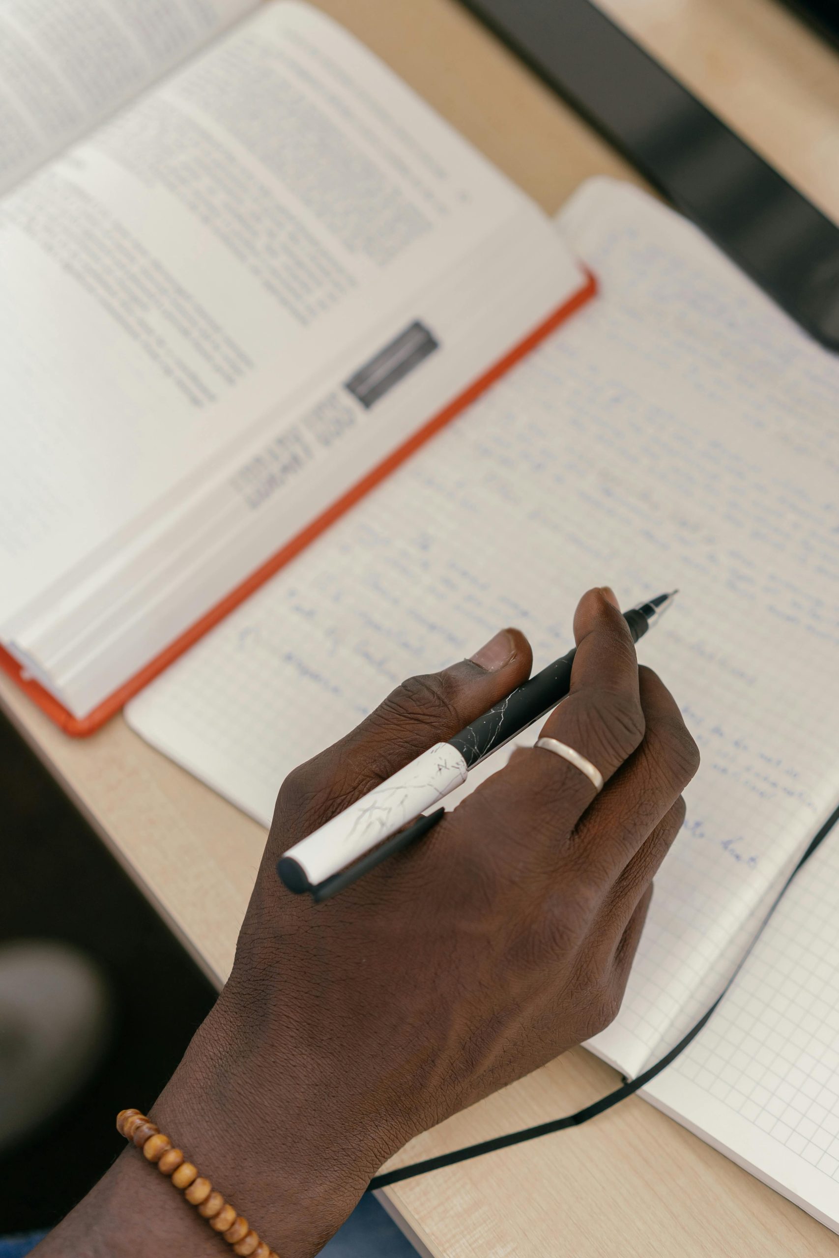 Picture of a hand holding a pen, over a book and paper